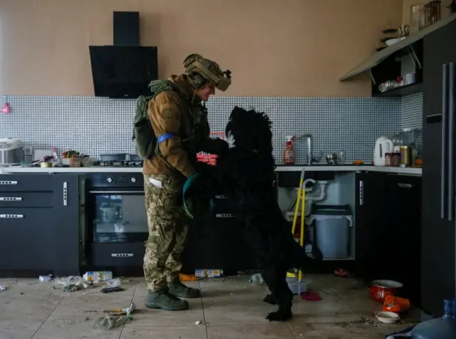 A Ukrainian soldier greets a dog abandoned by its owners inside a house on the frontline near Kyiv