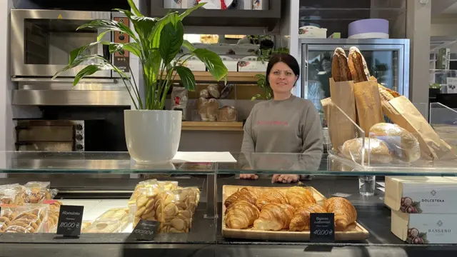 Woman stands behind counter with glass display filled with pastries in a cafe in Kyiv