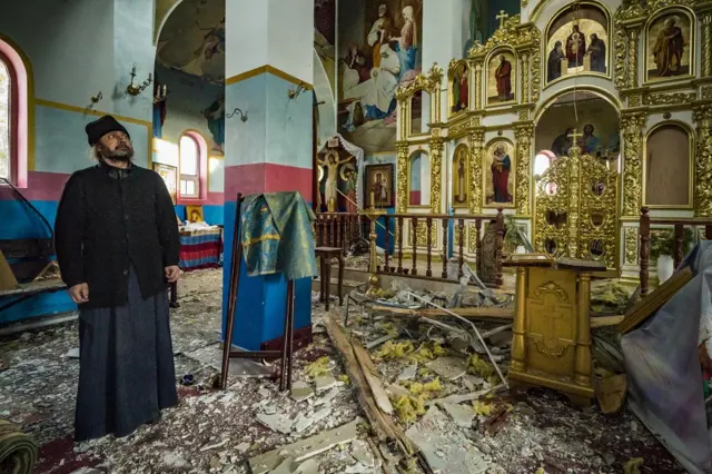 Priest Romanov of Yasnohorodka stands inside his damaged church