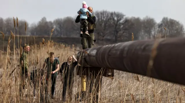 A soldier carries the baby of a displaced family across a river on the outskirts of Kyiv