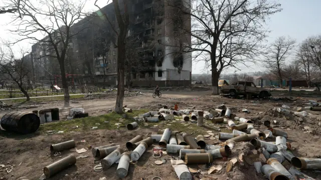 A boy rides a bike past shell casings in Mariupol, 31 March