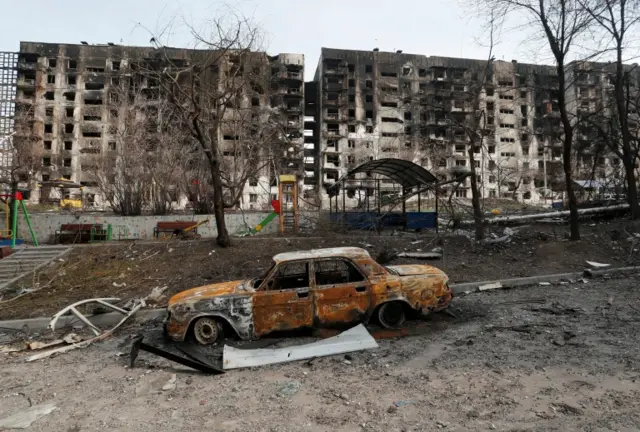 A charred car is seen in front of an apartment building destroyed during Ukraine-Russia conflict in the besieged southern port city of Mariupol