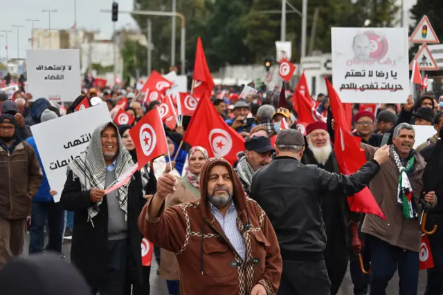 Tunisian protesters raise placards and national flags during a demonstration against their president