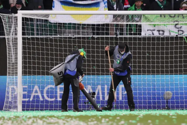 Staff try to clear confetti from pitch