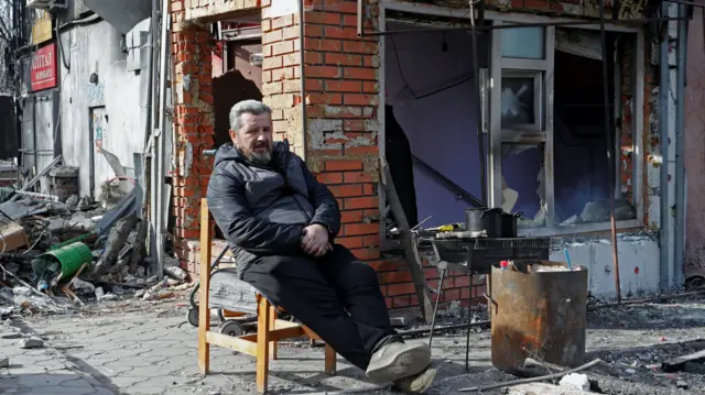 A Mariupol resident sits outside a damaged building, 31 March