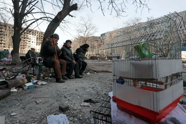 Residents site on a bench by a birdcage in Mariupol, 31 March