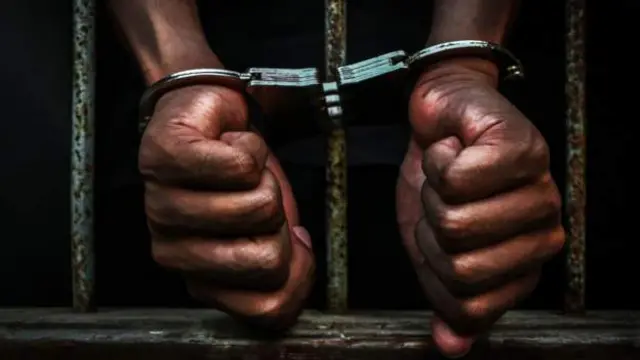 A stock image of a man handcuffed to the bars of a prison cell