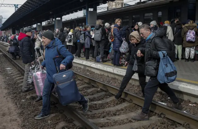 People at Kyiv railway station cross the tracks as they flee the city