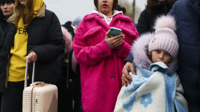 A child in a wooly hat and blanket walks with other adults across the Ukrainian-Polish border