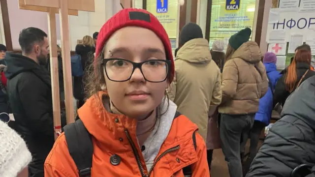 Mariana in an orange coat and red hat in a crowded Lviv station, Ukraine