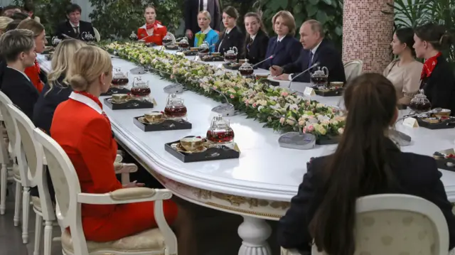 Putin sits round a long table of about 20 women from Aeroflot