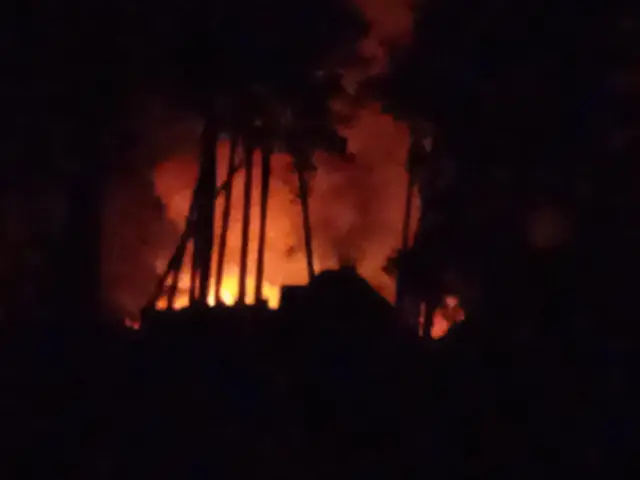 Flames and smoke rise from behind an unknown building, in a night-time picture