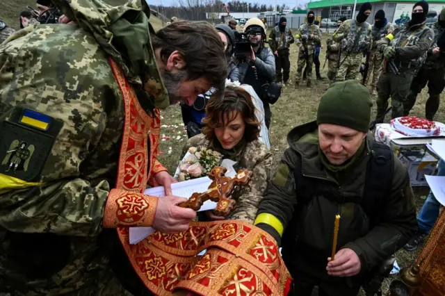 Lesya holds flowers, while Valery holds a candle