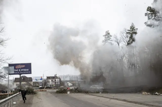 Someone runs away from a plume of smoke on the road from Irpin