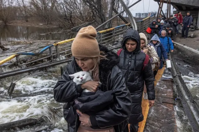 A woman with her cat crosses the destroyed bridge as residents flee from the frontline town of Irpin