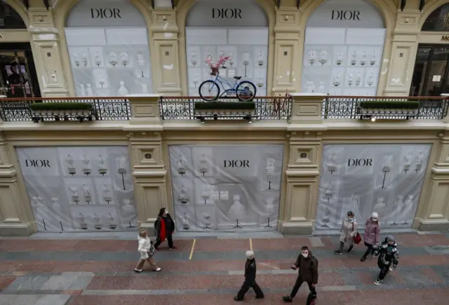 People walk past the windows of a closed Dior shop in Moscow