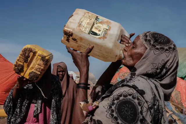 Hawa Mohamed Isack (R), 60, drinks water at a water distribution point at Muuri camp, one of the 500 camps for internally displaced persons (IDPs) in town, in Baidoa, Somalia, on February 13, 2022