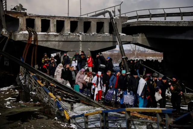 People walk across a makeshift river crossing below a destroyed bridge as they flee from advancing Russian troops in Irpin, west of Kyiv, Ukraine. Photo: 8 March 2022