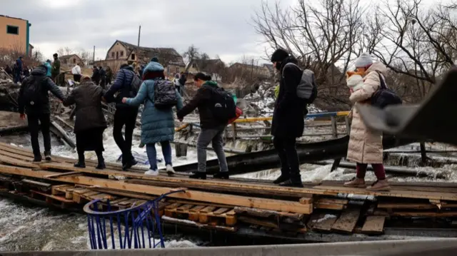 People fleeing advancing Russian forces file across wooden planks crossing Irpin River below a destroyed bridge as Russia"s attack on Ukraine continues in Irpin outside Kyiv, Ukraine,