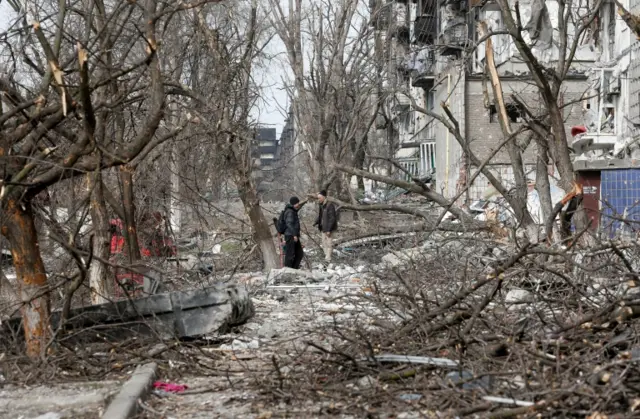 Men speak in a courtyard near a residential building damaged in Mariupol