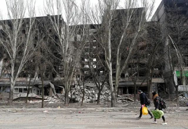 Civilians walk past a destroyed apartment building