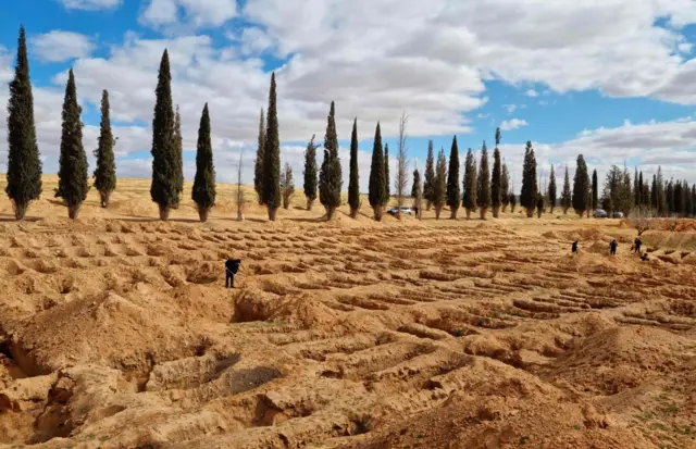 Libyans walk around graves dug on the ground from which bodies were recovered in the western town Tarhuna on February 9, 2022