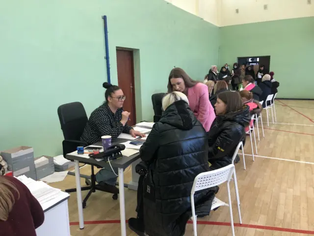 Rows of tables in the centre with refugees sitting at them to fill out paperwork