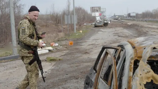 A soldier looks at a burned out car on a road