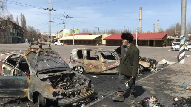 A man walks passed burnt out cars.