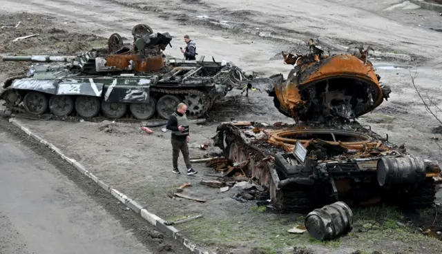 Residents look at a destroyed Russian tank on the outskirts of Buzova village, west of Kyiv