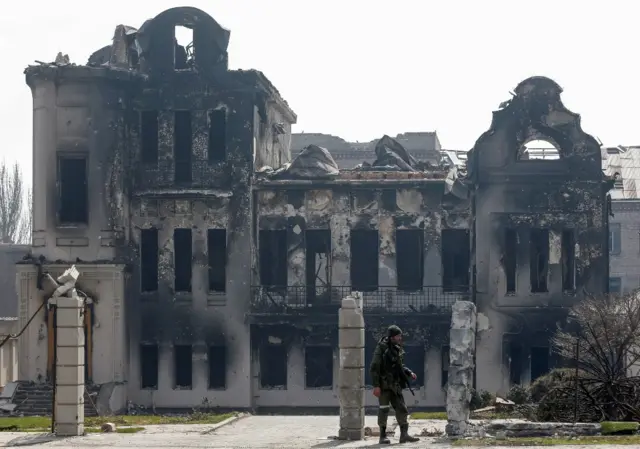 A service member of pro-Russian troops stands near a destroyed building in Mariupol