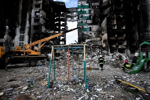 Rescuers search rubble of a residential building in Borodyanka, with child's swing visible in foreground