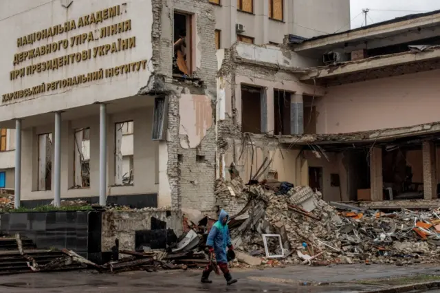 Woman walks past building destroyed by shelling in Kharkiv