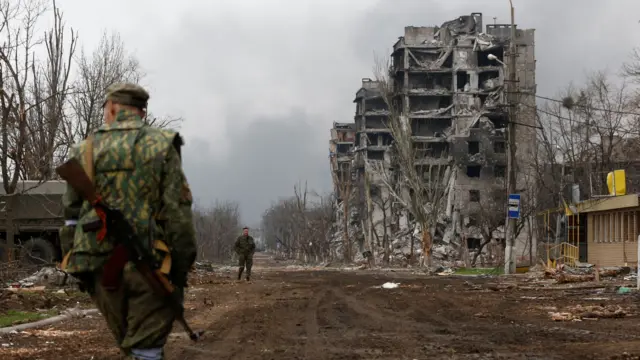 Pro-Russian troops walk in front of destroyed buildings in Mariupol