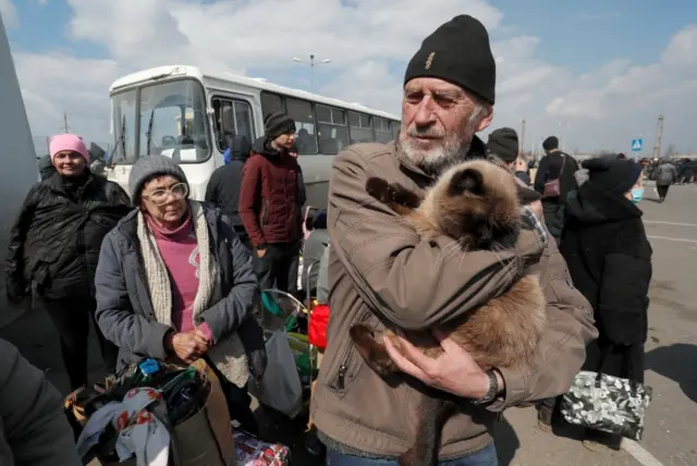 A man holds a cat as evacuees wait before boarding a bus