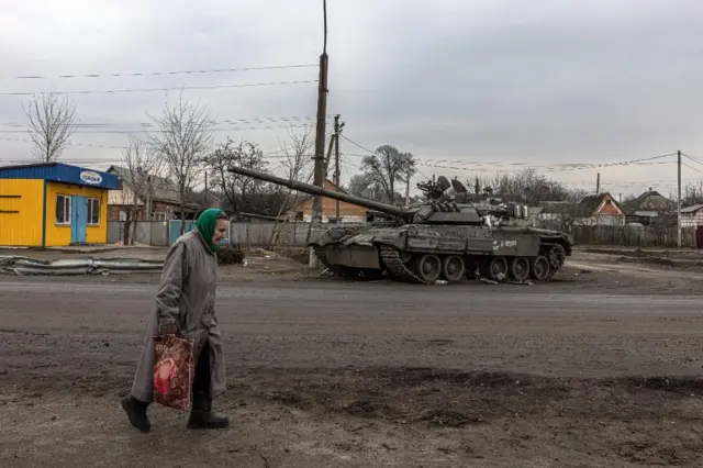 An elderly woman walks past a damaged Russian tank in a recaptured town in the Sumy region