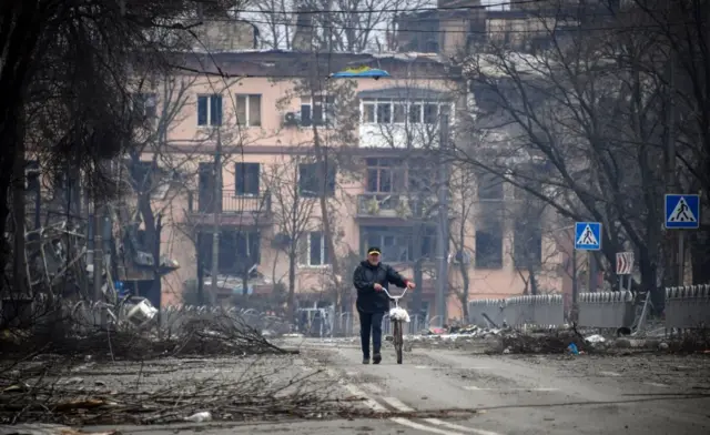 A man walks with a bicycle in downtown Mariupol as Russian troops intensify a campaign to take the strategic port city