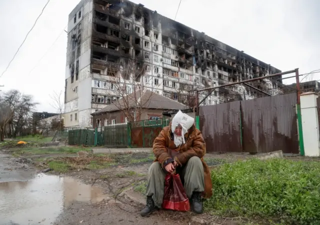 A woman in front of a ruined building