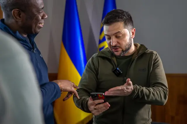 Zelensky gestures to his phone as Clive Myrie looks on