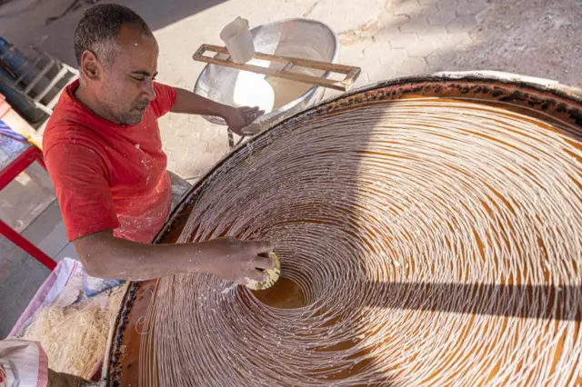 Egyptian confectioner Mostafa Anwar makes a traditional oriental dessert called "Kunafa" ahead of the fast-breaking "Iftar" meal, on the thirteenth day of the Muslim holy month of Ramadan, at his stall in the capital Cairo on April 14, 2022