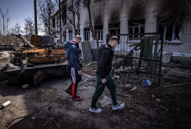 Men walk near a burnt armoured vehicle a damaged school in Bohdanivka village, northeast of Kyiv, on 14 April 2022