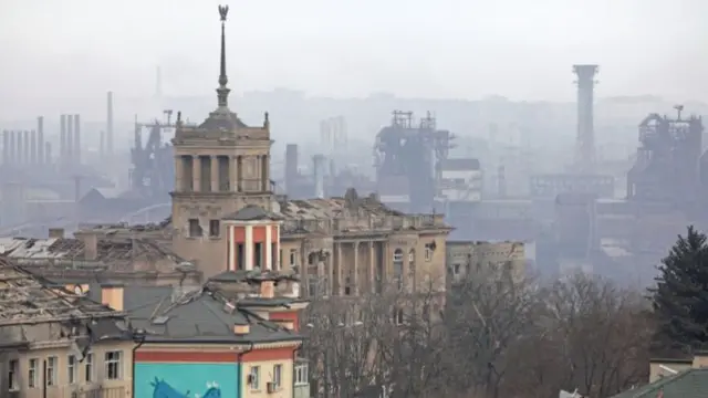 Damaged buildings stand in front of a clearly industrial area in this photo of Mariupol