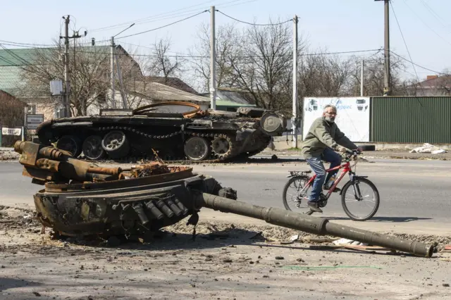 A man rides a bike near a destroyed Russian tank near Brovary, Kyiv