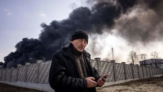 A man holds his smartphone outside a burning compound