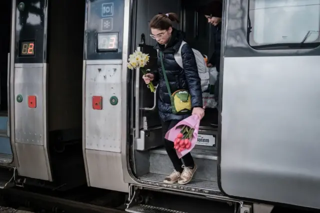 A woman holding flowers gets off a train arriving from Poland in Kyiv