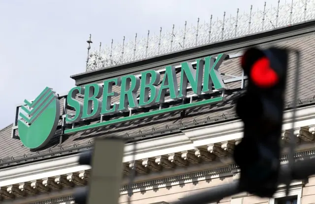 The logo of the Russian state-owned bank Sberbank is pictured next to a red traffic light, at its European subsidiary headquarters in Vienna on February 28, 2022.