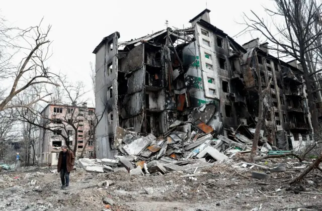 A man walks near a ruined residential building in Mariupol