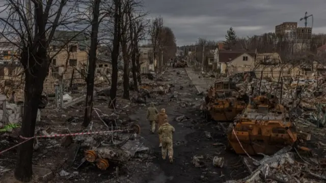 Members of the Ukrainian military walk past destroyed Russian military machinery on the street, in Bucha, the town which was retaken by the Ukrainian army, northwest of Kyiv