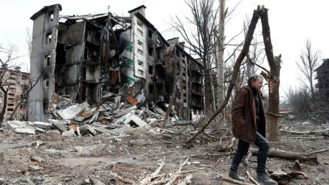 A man walks near a destroyed residential building in Mariupol