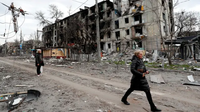 People walk past a damaged residential building in Mariupol